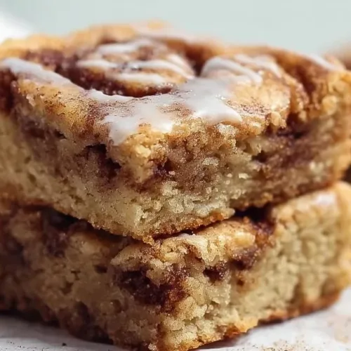 Freshly baked cinnamon roll blondies drizzled with icing on a wooden table.