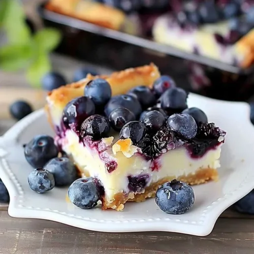 Delicious blueberry cheesecake bars topped with fresh blueberries and cream.
