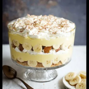 Banana Pudding Trifle with Vanilla Cream Filling 3 Delicious banana pudding trifle layered in a glass dish with banana slices and whipped cream.