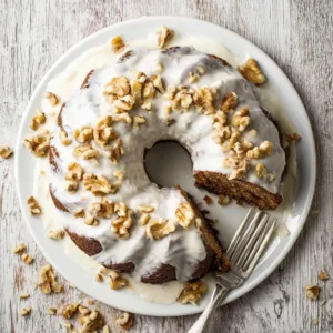 Delicious Hummingbird Bundt Cake topped with cream cheese frosting and garnished with nuts.